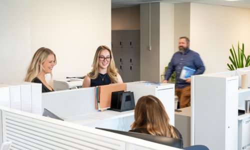 Des collègues discutent avec une autre collègue assise à son bureau.