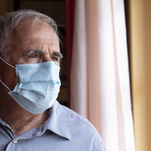 Vieil homme portant un masque regardant par la fenêtre