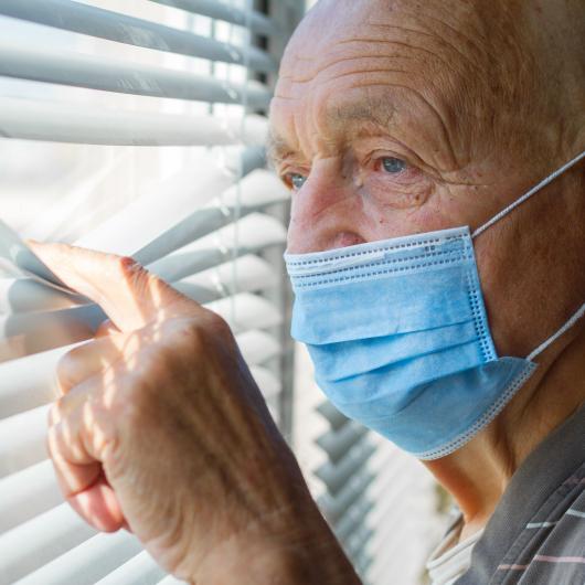Homme âgé portant un masque regardant à travers le store