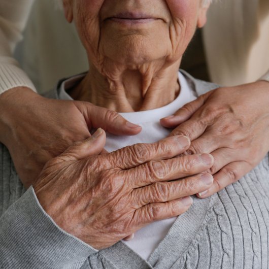 Dame âgée enlacée tendrement par un proche se tenant derrière elle