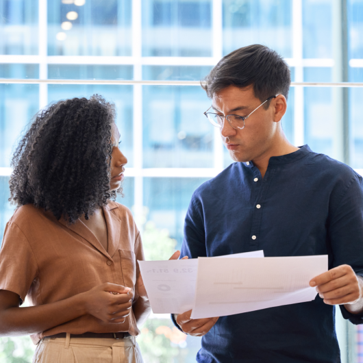 Deux collègues se tiennent debout côte à côte et discutent en regardant des documents.