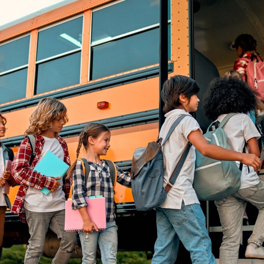 Enfants formant une file et s'apprêtant à monter dans un autobus scolaire.
