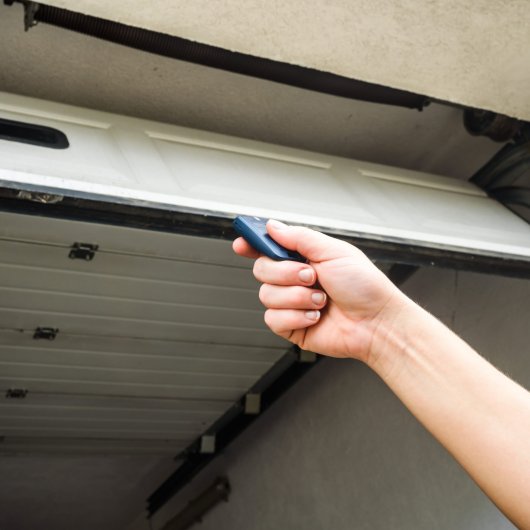 Main tenant une manette devant une porte de garage ouverte.